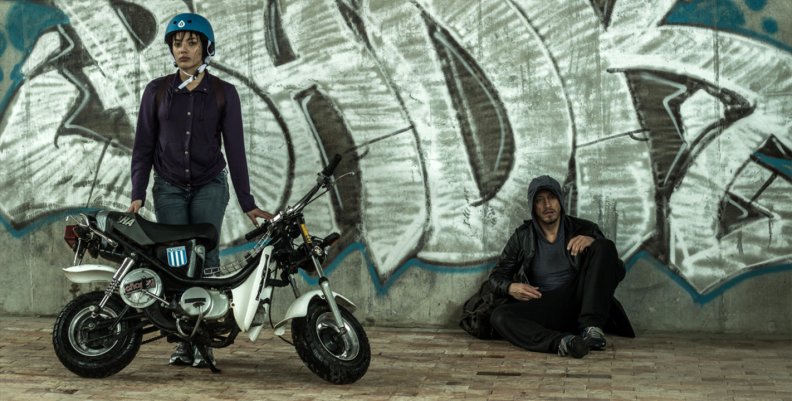 Película 'Destinos' por Canal Capital Dos personas, una mujer con casco y moto, un hombre sentado contra una pared.