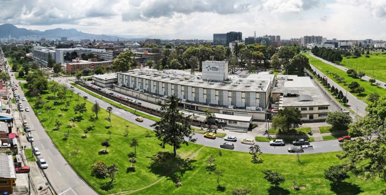 Vista panorámica de un hospital: fachada blanca con gris, rodeado de árboles y césped Hospital Universitario de Colombia