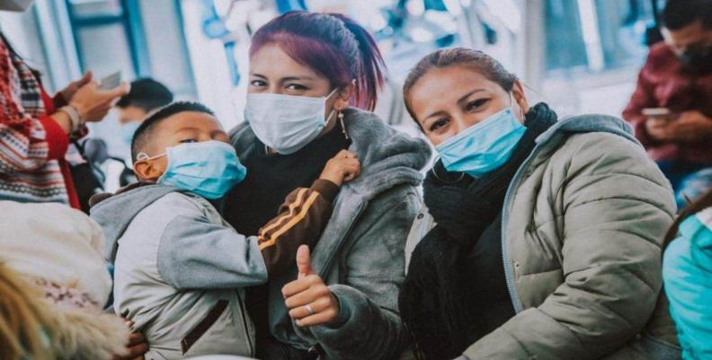Mujeres con tapabocas. Una lleva en brazos a un niño