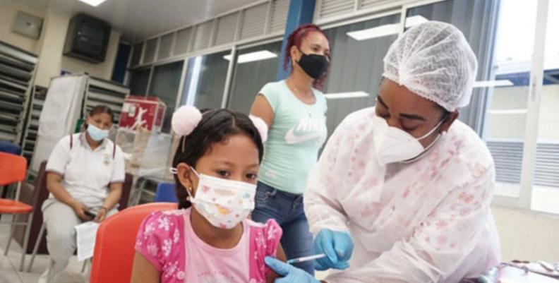 Enfermera vacunando a una niña. Ambas portan tapabocas
