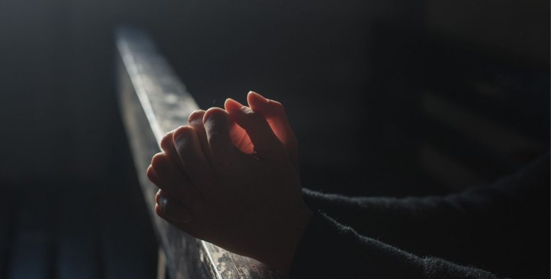 Religión Unas manos rezando sobre una banca de madera