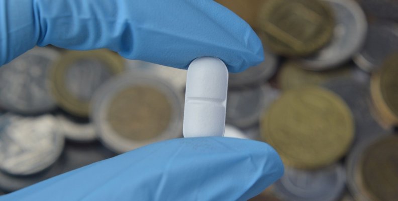 Desabastecimiento de medicamentos Una mano con guante azul sosteniendo una pastilla blanca