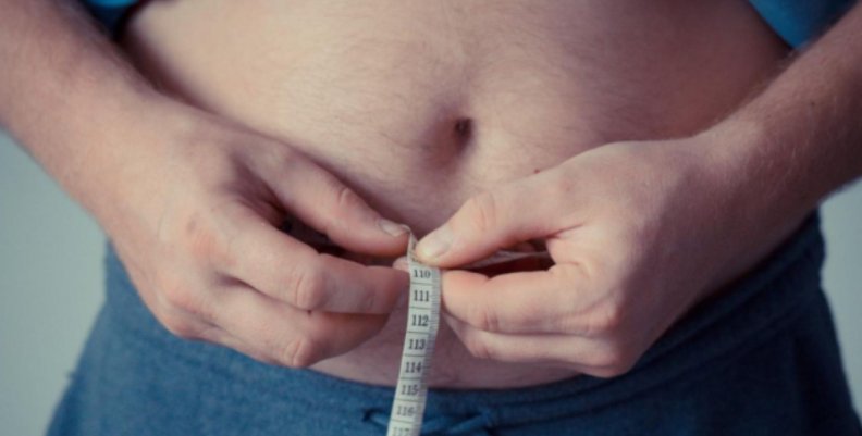 Sobrepeso Hombre midiéndose el diámetro de la cintura con una cinta métrica
