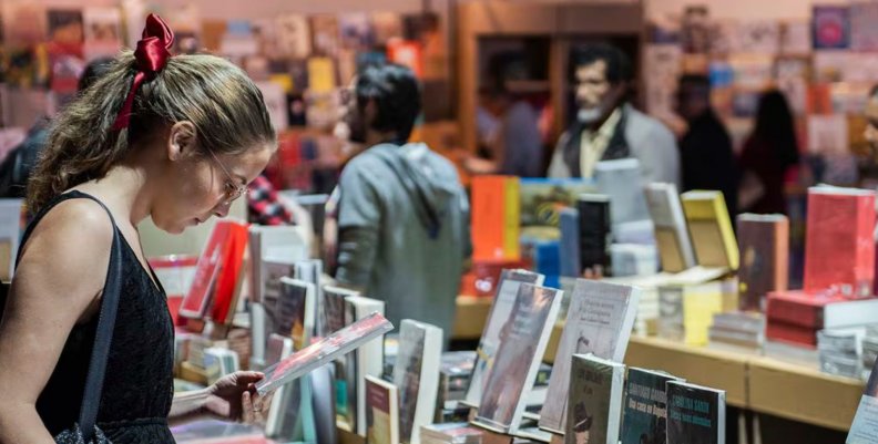 Mujer en la Feria de Libro de Bogotá viendo libros Efemérides literarias de la FILBo 2024: un viaje a través de la historia de la literatura
