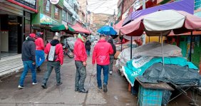 Cuatro hombres con chaquetas rojas caminando sobre una calle llena de puestos de venta ambulante