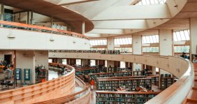 Pasillos con suelo de madera y paredes blancas: en medio, estantes de libros