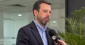 Hombre con traje negro y camisa azul hablándole a un micrófono