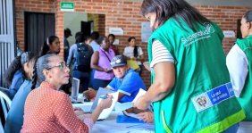 Mujer con chaleco verde hablando con otra mujer sentada en una mesa