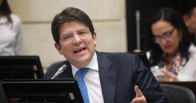 Un hombre con traje negro, camisa blanca y corbata azul en un escritorio