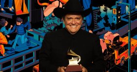 Un hombre con traje negro llanero, sombrero y un grammy en las manos