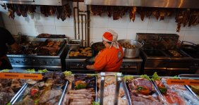 Cocina con una cocinera en el medio y rodeada de diversos ingredientes 