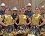 Hombres y mujeres con trajes típicos: mujeres con vestidos dorados y negros y hombres con camisas negras y sombreros