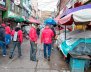 Cuatro hombres con chaquetas rojas caminando sobre una calle llena de puestos de venta ambulante
