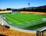 Vista panorámica de un estadio con gradas rojas y amarillas y césped verde en el medio