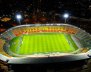 Vista panorámica de un estadio. Las gradas son amarillas con rojo y hay una chancha de fútbol en el medio