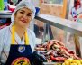 Una mujer con mantel y cofia delante de una mesa llena de fritanga