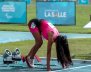 Atleta vestida de rosado en posición de salida. Está encima de un partidor de metal y una pista atlética azul