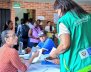 Mujer con chaleco verde hablando con otra mujer sentada en una mesa