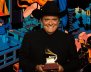 Un hombre con traje negro llanero, sombrero y un grammy en las manos