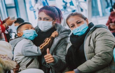 Mujeres con tapabocas. Una lleva en brazos a un niño