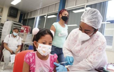 Enfermera vacunando a una niña. Ambas portan tapabocas