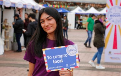 Mujer con camiseta morada sosteniendo un cartel de Hecho en Bogotá