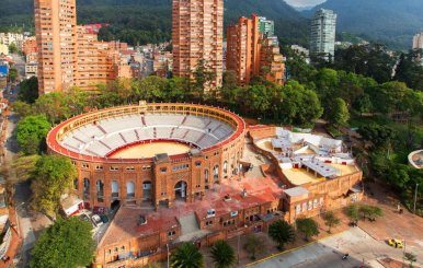 Plaza de toros color ladrillo. Atrás hay unas torres de apartamentos