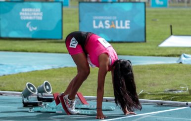 Atleta vestida de rosado en posición de salida. Está encima de un partidor de metal y una pista atlética azul