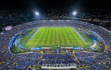 Vista panorámica de un estadio de fútbol. Los hinchas visten prendas azules y el cielo está de noche