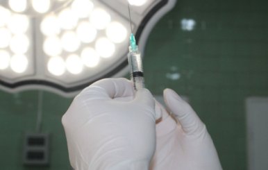Manos con guantes quirúrgicos que sostiene una aguja hipodérmica