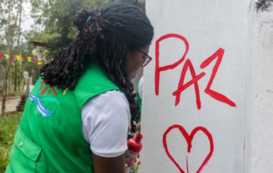 Mujer haciendo un grafiti que dice "Paz" en una pared blanca