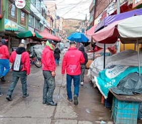 Cuatro hombres con chaquetas rojas caminando sobre una calle llena de puestos de venta ambulante