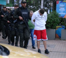 Policías armados custodiando a un hombre con hoodie blanco y shorts rojos