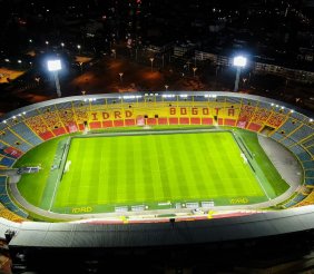Vista panorámica de un estadio con gradas rojas y amarillas y césped verde en el medio